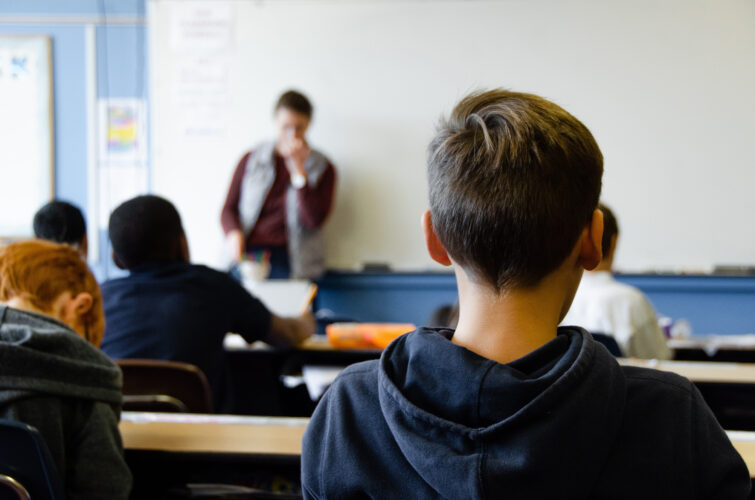teacher leans on white board in front of students