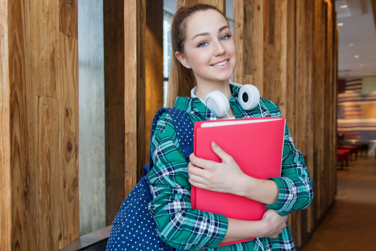 smiling teen with headphones and red notebook
